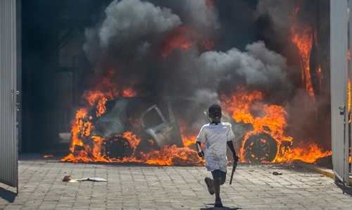 Seorang anak laki-laki berlari menjauh dari sebuah dealer mobil yang dibakar para pengunjuk rasa di Port-au-Prince, Haiti, 17 Maret 2021.(VOA)