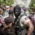 Orang-orang bersorak ketika mobil polisi melewati kantor Polisi Petionville di mana orang-orang bersenjata, yang dituduh terlibat dalam pembunuhan Presiden Jovenel Moise, ditahan di Port au Prince, Haiti, pada (8/7/2021). [Valerie Baeriswyl / AFP]