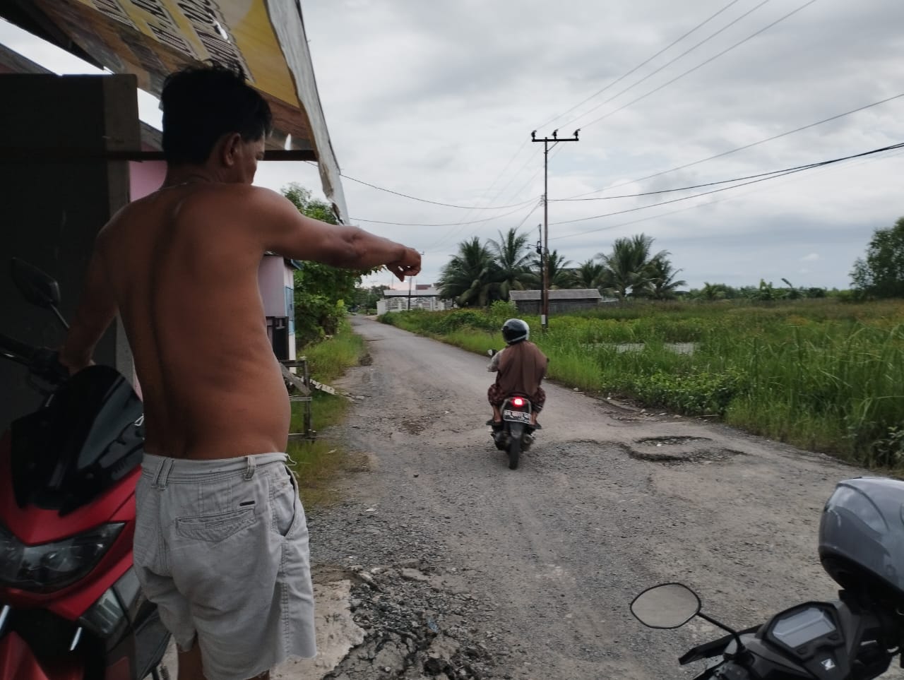 Salah seorang warga Desa Simpang Warga Kecamatan Aluh-Aluh Kabupaten Banjar bernama Asrul (Asul) menunjuk jalan yang rusak berlubang di depan rumahnya, Minggu (7/7/2024). (Foto: Leon/Koranbanjar.net)